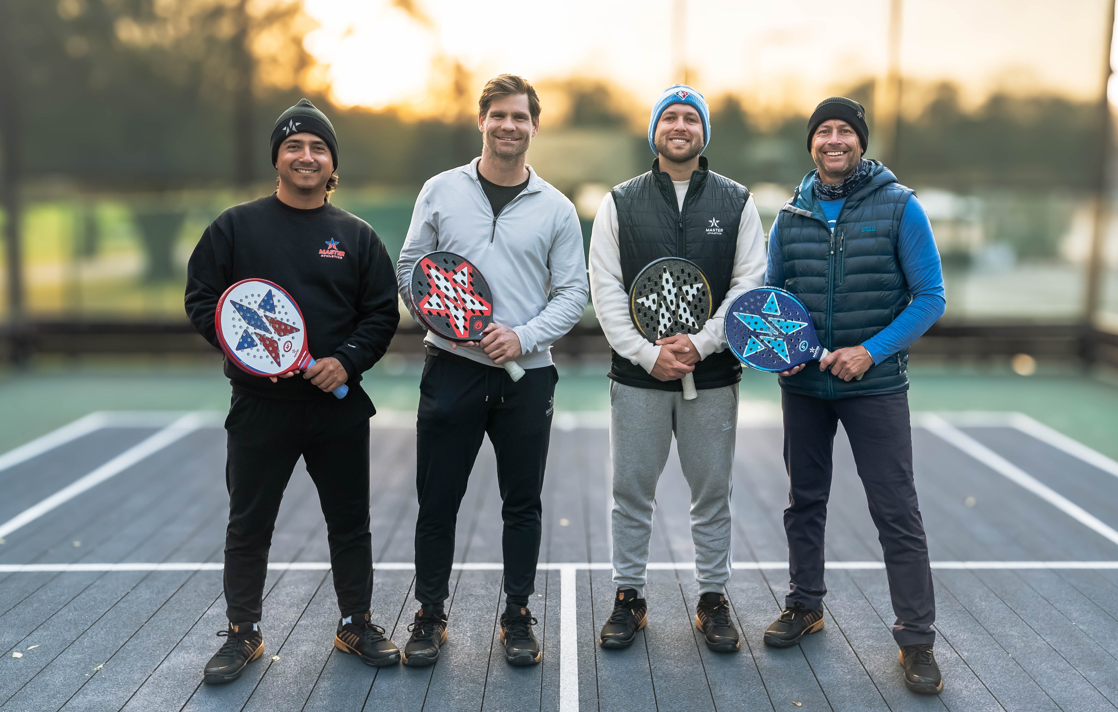 Four men holding paddle sports equipment on a court with a sunset background